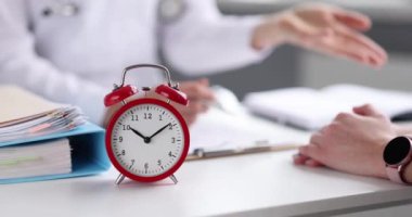 Doktor ve hastanın masasında duran kırmızı alarmlı saat 4K 'lık filmi yavaş çekimde kapatıyor. Klinik açılış saatleri kavramı