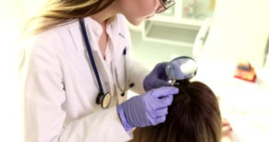 Dermatolog trikoloğu kadın kıllarını büyüteçle inceliyor. Kadınlarda saç dökülmesi sorunu