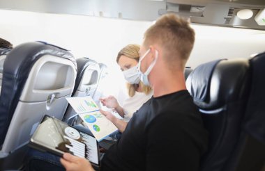 Koruyucu maskeli bir adam ve bir kadın uçakta belgeleri olan, yakın plan. Uçuş toplantısı, iş gezisi.