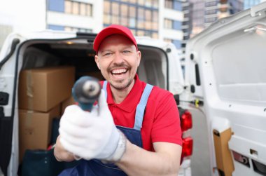 Kırmızı üniformalı bir kurye kapalı bir minibüsün yanında bir alet gösteriyor, yakın plan, bulanık. Kargo taraması, posta hizmetleri