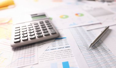 Masada bir hesap makinesi, kalem ve finansal belgeler var, yakın plan. Finansörün işyeri, gelir ve giderlerin hesaplanması