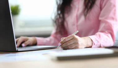 Kadın kalem kâğıt ve dizüstü bilgisayarla notlar alıyor. Atmosfer aktivitesi verimli bir işe çok yardımcı olur. İyi bir uzman ana işi yapmayı başarır. İş yükü çok fazla.