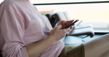 Kadın akıllı telefonu tren istasyonunda ya da havaalanında otururken tutuyor. Bilet rezervasyonu ve seyahat programı için mobil uygulama