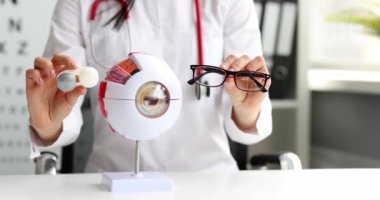 Doktor göz doktoru, insan gözünün maketinin arka planında gözlük ve kontak lensler tutuyor. Göz konsepti için optik seçimi