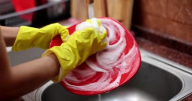 Eldivenli köpüklü sünger kırmızı tabağı yakın mesafeden yıkar. Evde bulaşık deterjanı