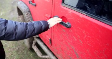 Erkek sürücü toprak yolda kirli kırmızı 4x4 SUV 'nin kapısını açıyor. Off road dağ safarisi ve macera