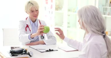 Doktor endokrinolog, klinikteki yaşlı kadın hastaya ağır çekimde yeşil elma veriyor. Yaşlılık kavramında rasyonel beslenme