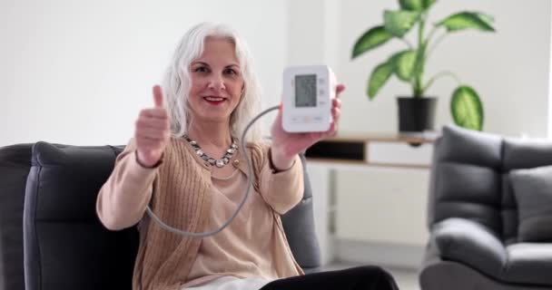 灰色の髪をしている高齢者の女性は ホーム4K映画スローモーションで通常の血圧で親指とクロノメーターを表示します 高齢者における動脈性高血圧の治療の概念 — ストック動画