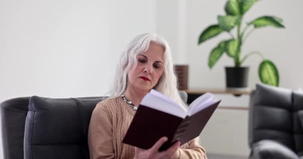 Starsza Kobieta Siwymi Włosami Siedząca Fotelu Domu Czytająca Książkę Film — Wideo stockowe