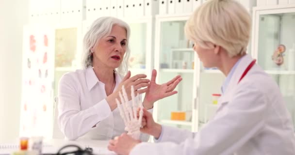Γιατρός Ρευματολόγος Δείχνει Ανατομικό Μοντέλο Του Ανθρώπινου Χεριού Ηλικιωμένη Γυναίκα — Αρχείο Βίντεο