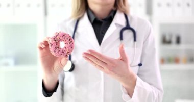 Kadın doktor elinde tatlı bir donut tutuyor. Yakın çekim 4K film ağır çekim. Diyet ve uygun beslenme konsepti