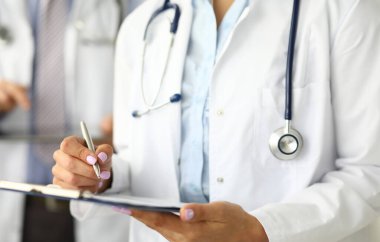 Pratisyen hekimin elleri hastanede yakın planda tutulan önemli bir belgeyi imzalıyor.