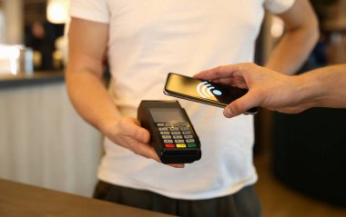 Müşterilerin kafedeki terminal ve cep telefonlarıyla ödeme yaptıkları yakın çekim. Akıllı telefonla öde. Bağlantısız NFC ve modern cihaz teknolojisi kavramı