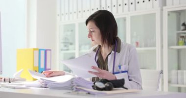 Hasta muayene kâğıdı belgelerini inceleyen kadın doktor. Ağır çekimde 4K film. Tıp konseptinde evrak işi