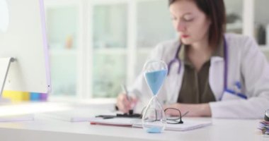 Klinikte çalışan doktorun arka planındaki kum saati. Yakın çekim 4K film ağır çekim. Klinik muayene kavramı