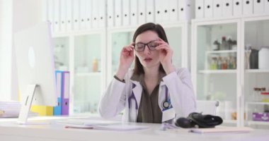 Uykulu yorgun doktor, klinik 4K filminde ağır çekimde masada gözlüklerini çıkarıyor. Klinik konseptinde doktor çalışmasında zorluklar
