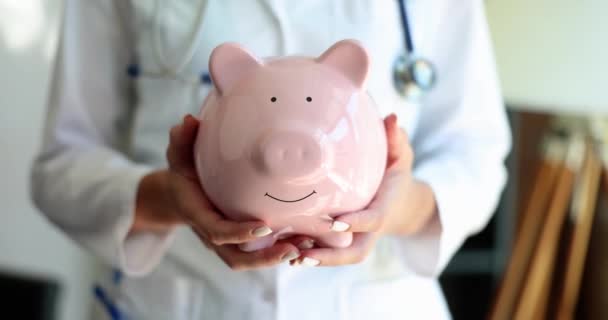 Médica Mulher Segurando Banco Porquinho Clínica Poupando Dinheiro Cuidados Médicos — Vídeo de Stock
