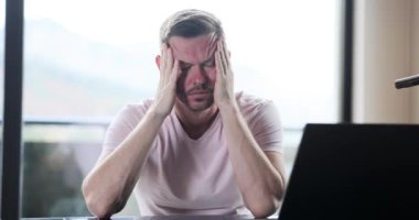 Dizüstü bilgisayarla çalıştıktan sonra çok kötü baş ağrısı çeken stresli bir adam. Kronik migrenden muzdarip yorgun serbest çalışan