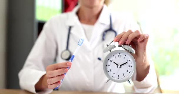 歯医者は口腔衛生の間 歯ブラシと目覚まし時計を手に持っています 歯科病院で働く歯科医 — ストック動画