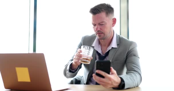 Αναστατωμένος Επιχειρηματίας Πίνοντας Αλκοόλ Στο Χώρο Εργασίας Και Κοιτάζοντας Smartphone — Αρχείο Βίντεο