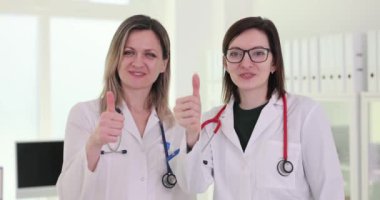 Kadın doktorlar, klinik 4K filminde yavaş çekimde başparmak gösteriyor. Tıp alanında başarılı bir kariyer.