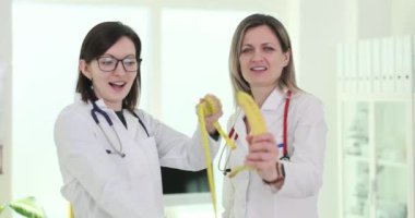 Female doctors showing banana penis and measuring tape in clinic 4k movie slow motion. Treatment of infertility and impotence concept