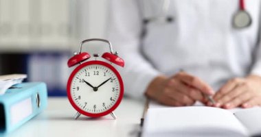 Red alarm clock stands at workplace of doctor. Deadline for end of seasonal illness or pandemic.