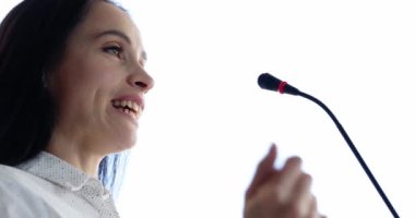 Woman speaker speaks into microphone gesturing with hands. Holding business conference concept