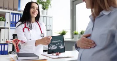 Gynecologist shows ultrasound scan of fetus to pregnant woman at medical appointment.
