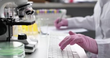 Scientist types on keyboard and takes notes on documents in laboratory. Work and education of doctors and scientists concept