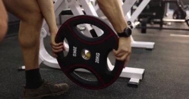 Sporcu halter için diski 20 kg 'lık spor salonunda rafa kaldırıyor. Yakın çekim 4K film yavaş çekim. Güç yükü el konseptine