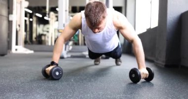 Spor salonu 4K filminde dambıllarla şınav çeken erkek sporcu. Vücut konsepti için düzenli sıralama yükü