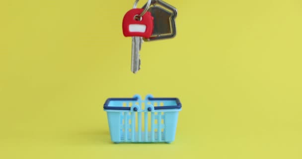 黄色い背景のクローズアップ4K映画の食料品のためのおもちゃのバスケットに家の鍵を入れて女性の手 物件概念の購入 — ストック動画