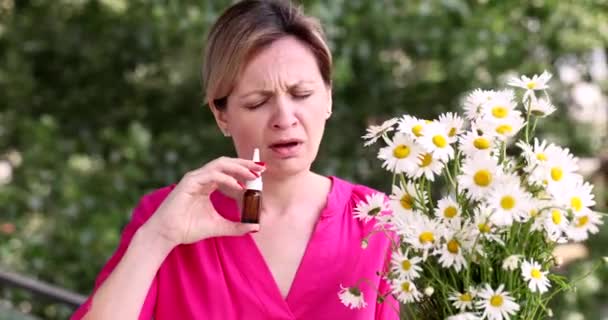 有花粉热的女人闻到洋甘菊花的香味 并在4K电影外的小瓶里滴了些水滴在鼻子里 季节性过敏和支气管哮喘概念 — 图库视频影像