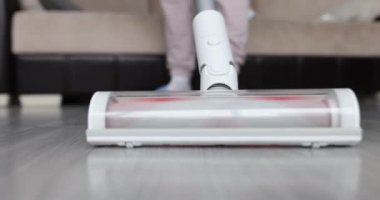 Kadın modern oturma odasında kablosuz elektrik süpürgesiyle yerleri süpürüyor. Kablosuz elektrik süpürgesi konseptiyle kolay temizlik