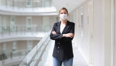 Takım elbiseli ve koruyucu tıbbi maskeli genç bir kadın otelin koridorunda duruyor. Covid19 salgını sırasında otel müşteri hizmetleri