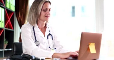 Odaklanmış doktor bir hastanede masada oturuyor ve internette dizüstü bilgisayarla çalışıyor. Bilgisayar ekranına bakan konsantre kadın hemşire ya da pratisyen hekim.