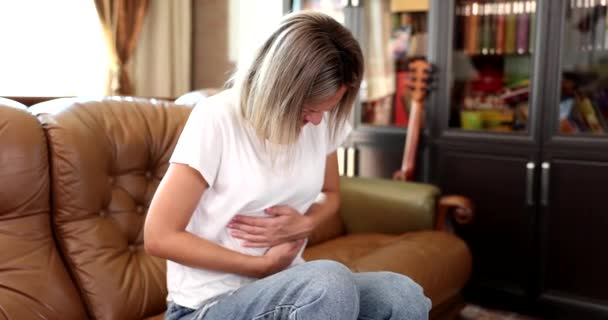 胃の痛みが激しいため 女性は手で胃をつつくソファに座っています 下痢性胃炎 リビングルームでの腸炎 人々の健康問題の概念を持つ女の子 — ストック動画