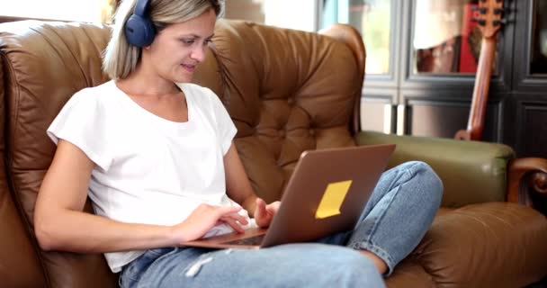 ソファの教育にヘッドフォンやラップトップを持つ女性がリモートで 自立した社会的距離とオンライン教育言語コースで自宅から仕事 — ストック動画