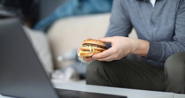 Erkek elinin sağlıksız sandviçi tutmasına ve hızlı karbonhidratlar ve zararlı kalorilerle dolu yağlı bir yemek yemeye hazırlanmasına odaklan. Zararlı fast food konsepti