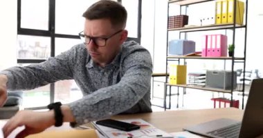Ofis 4K filminde gözlüklü bir işadamı masaüstünde belge arıyor. İş konseptinde kağıtlar