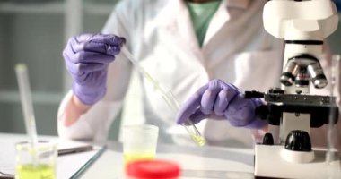 Laboratuvar asistanı bir pipetle birlikte bir mataraya sarı bir sıvı döküyor, yakın plan. Laboratuvar testleri, tanı testleri