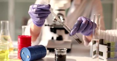 Laboratuvar asistanı şişeye siyah sıvı dolduruyor, yakın plan. Yakıtın kimyasal incelemesi