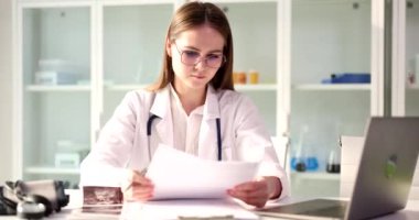 Genç doktor belgeleri tutuyor ve dizüstü bilgisayara bakıyor. Hasta analizi, sağlık teşhisi
