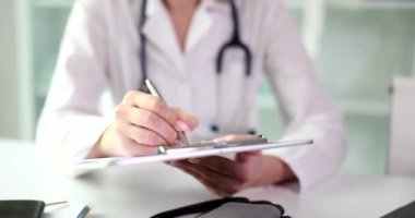 Masada oturan doktor beyaz bir klasöre yakın çekim yazıyor. Terapiste bir ziyaret, hasta kartı.