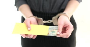 Elleri kelepçeli bir kadın bir zarftan dolar çıkarır, elleri yakın çekimde. Rüşvet, yasadışı para