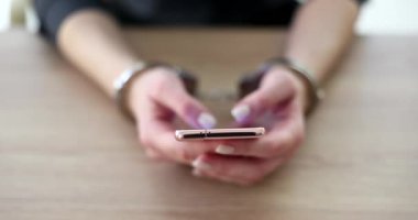 Elleri kelepçeli bir kadın akıllı telefonu kaydırıyor, elleri kapalı. Tutuklandığında telefon görüşmesini algıla, yavaş çekim