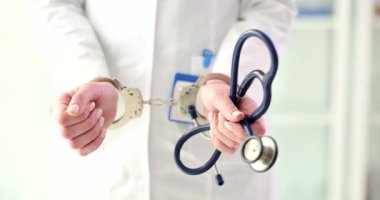 Elleri kelepçeli sıhhiye steteskop tutuyor, elleri yakın çekim. Tıbbi personelin tutuklanması, hata doktoru