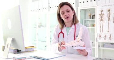 Kadın bir cerrah, ayağın anatomik modelini tutuyor. Yakın plan. Bir nörologun muayenesi, zaman ayarlı.