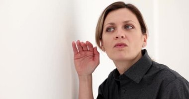 Bir iş kadını bir duvarın arkasından gizlice dinliyor, yakın plan. Gizli bilgi, merak.